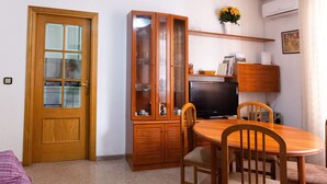 Een kleine woonruimte met een houten eettafel, stoelen, een televisie, een kast met glazen deuren en een deur.