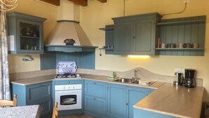A kitchen with blue cabinets, a gas stove, an oven, a sink, and a coffee maker.