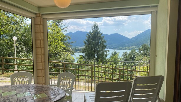 A balcony with a table and chairs, overlooking a lake and mountains.