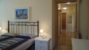 A bedroom with a bed, bedside tables, a lamp, a painting, and a door leading to another room.