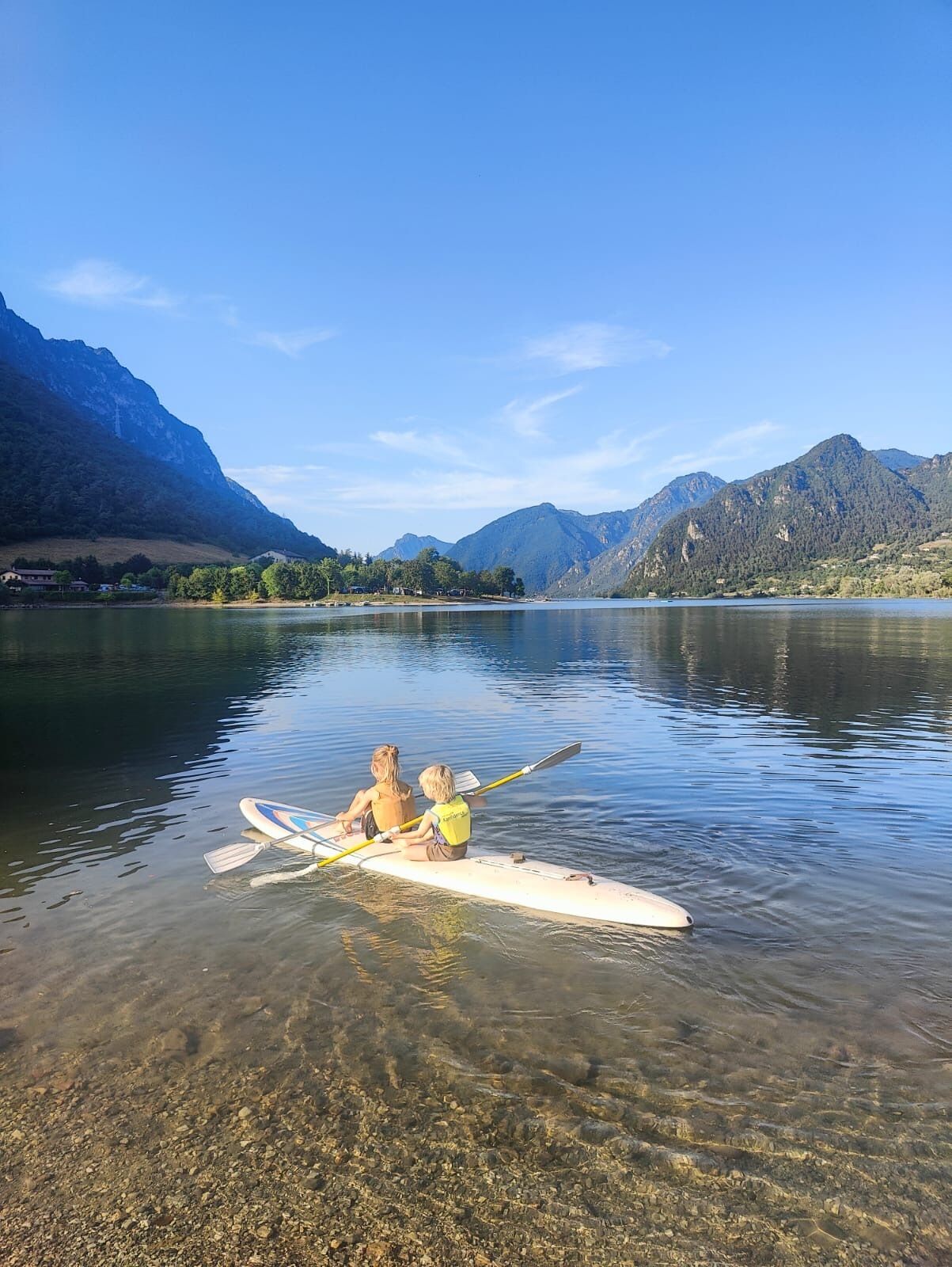A calm lake with two people rowing a boat, surrounded by mountains and clear skies.
