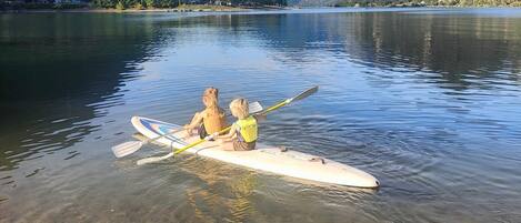 A calm lake with two people rowing a boat, surrounded by mountains and clear skies.