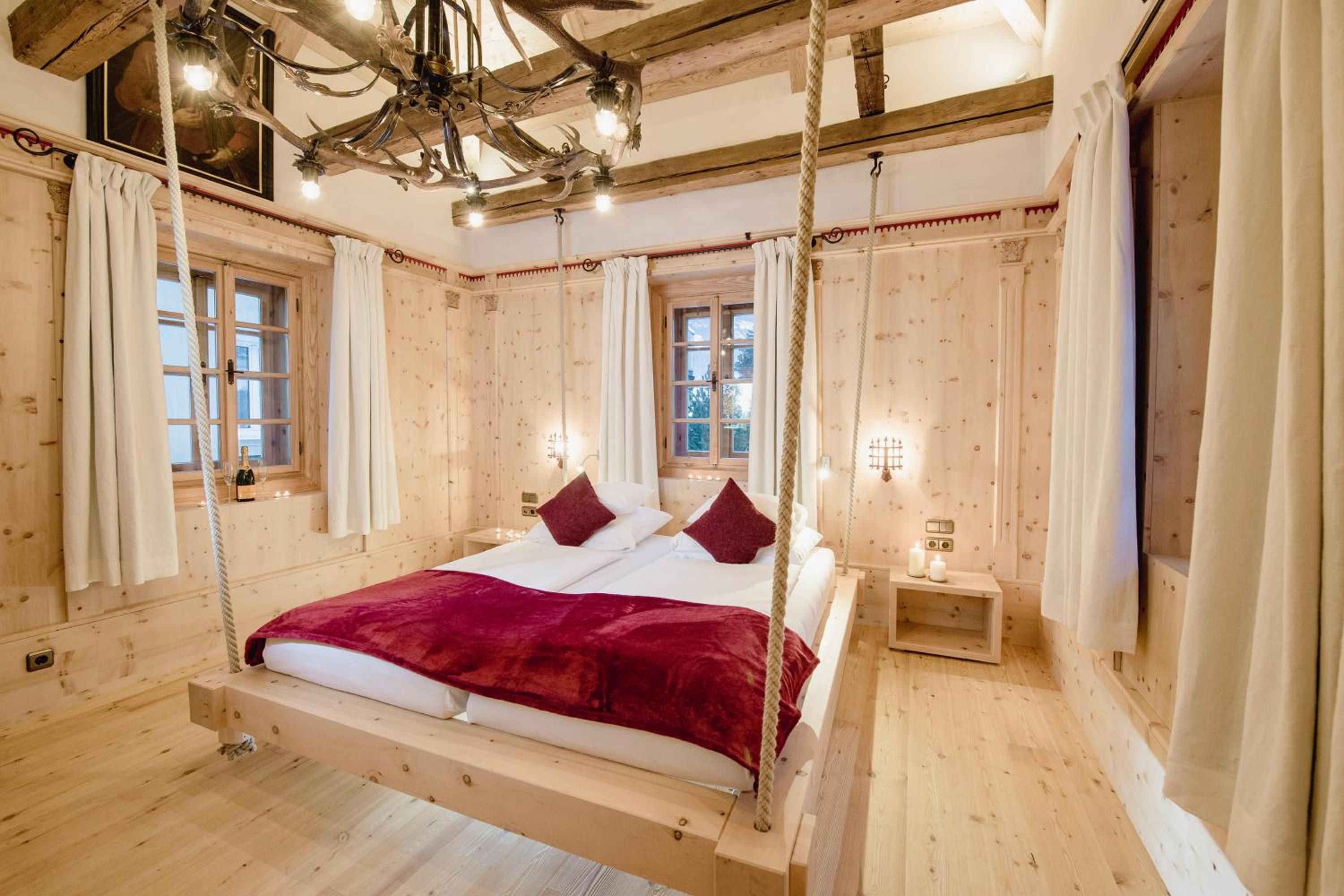 Ein Zimmer aus Holz mit einem an Seilen aufgehängten Bett, Holzwänden und einer Chandelier.