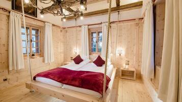 Ein Zimmer aus Holz mit einem an Seilen aufgehängten Bett, Holzwänden und einer Chandelier.