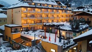 A multi-story hotel with a snow-covered roof and balconies, surrounded by other buildings and a mountainous backdrop. - Norica Hotel (Bad Hofgastein)
