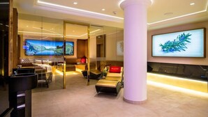A modern lobby with a large TV, comfortable seating, and a reception desk. - Norica Hotel (Bad Hofgastein)