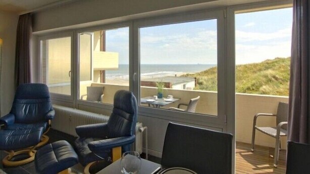 A balcony with a view of the beach and dunes. There are two blue chairs and a table with a lamp. - Wooge Traum - With sea view directly on the beach (Wangerooge)