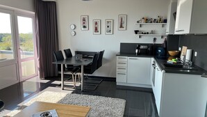 A modern kitchen with a dining area, featuring a large window, black and white cabinetry, and a view of greenery outside. - Wooge Traum - With sea view directly on the beach (Wangerooge)