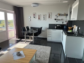 A modern kitchen with a dining area, featuring a large window, black and white cabinetry, and a view of greenery outside.