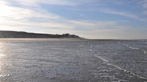 A beach with a building on a hill in the background. - Wooge Traum - With sea view directly on the beach (Wangerooge)