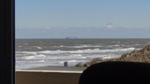 A view of the ocean with rough waves and a ship in the distance. - Wooge Traum - With sea view directly on the beach (Wangerooge)