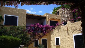 Un patio con un muro de piedra, un edificio con una torre de piedra y una escalera que conduce a un balcón.