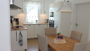 A modern kitchen with white cabinets, a wooden dining table, and pendant lighting. - F86 - balcony, close to the Bodden, Baltic Sea 6 km away, WLAN (Born)