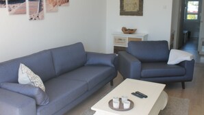 A living room with a grey sofa, a matching armchair, and a coffee table with remote controls and cups. - F86 - balcony, close to the Bodden, Baltic Sea 6 km away, WLAN (Born)