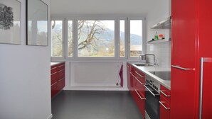 Une cuisine moderne avec des meubles rouges, un plan de travail blanc et une grande fenêtre donnant sur un paysage montagneux.
