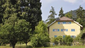 Ein gelbes Gebäude mit blauen Fensterläden, umgeben von Bäumen und einem Holzzaun.