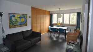 Un salon moderne avec un canapé foncé, une table à manger avec des chaises et une grande fenêtre avec des rideaux.