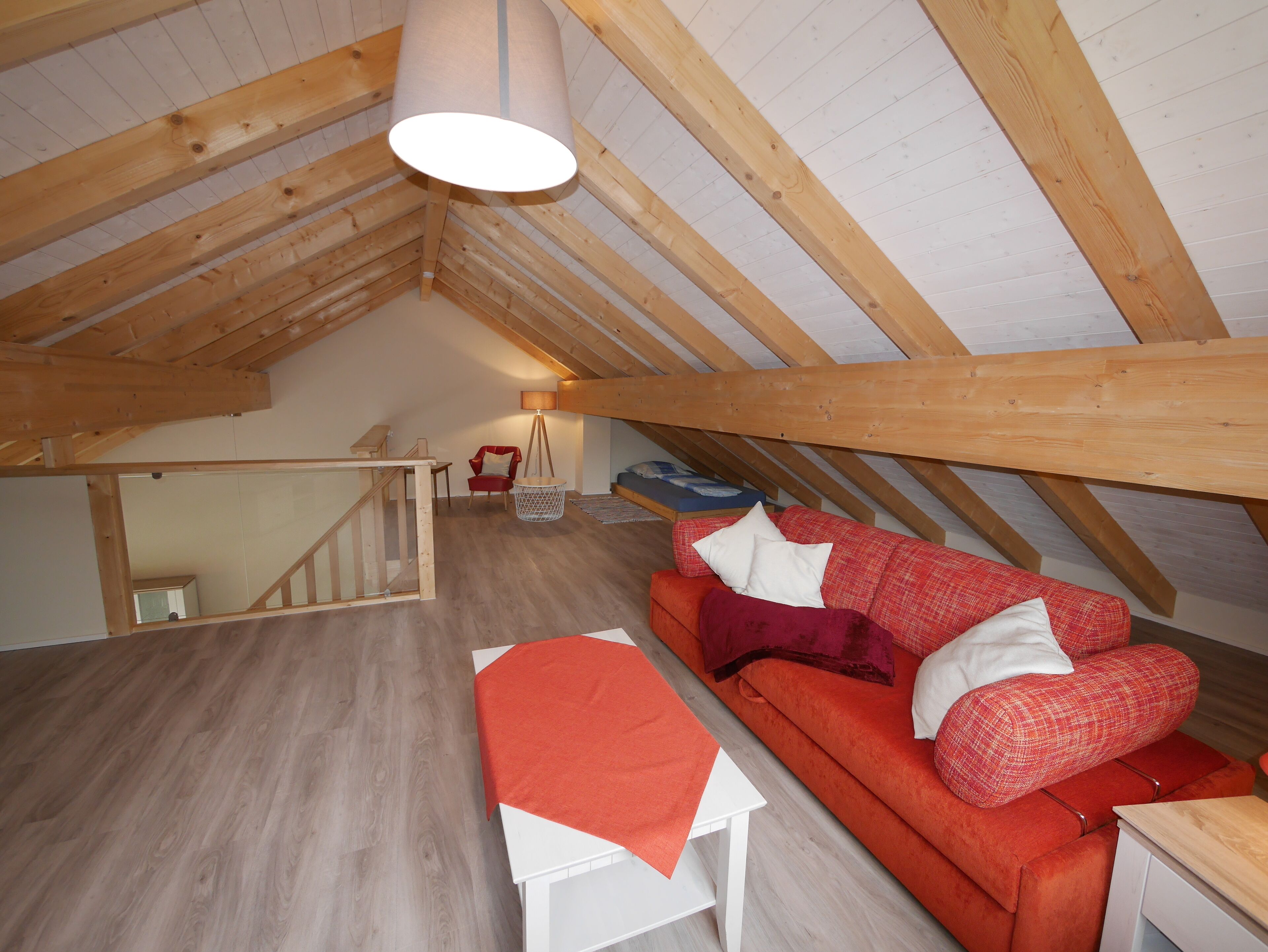 A loft bedroom with a wooden ceiling, a red sofa, a white table, and a hanging lamp.
