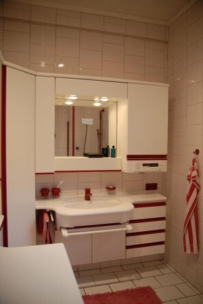 A bathroom with a white sink, mirror, and cabinets. There are red accents on the cabinets and a red towel hanging on the wall. - detached holiday house, calmly located in an olive grove (Thessalien)