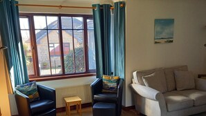 A living room with a sofa, two armchairs, a small table, and a large window with curtains.