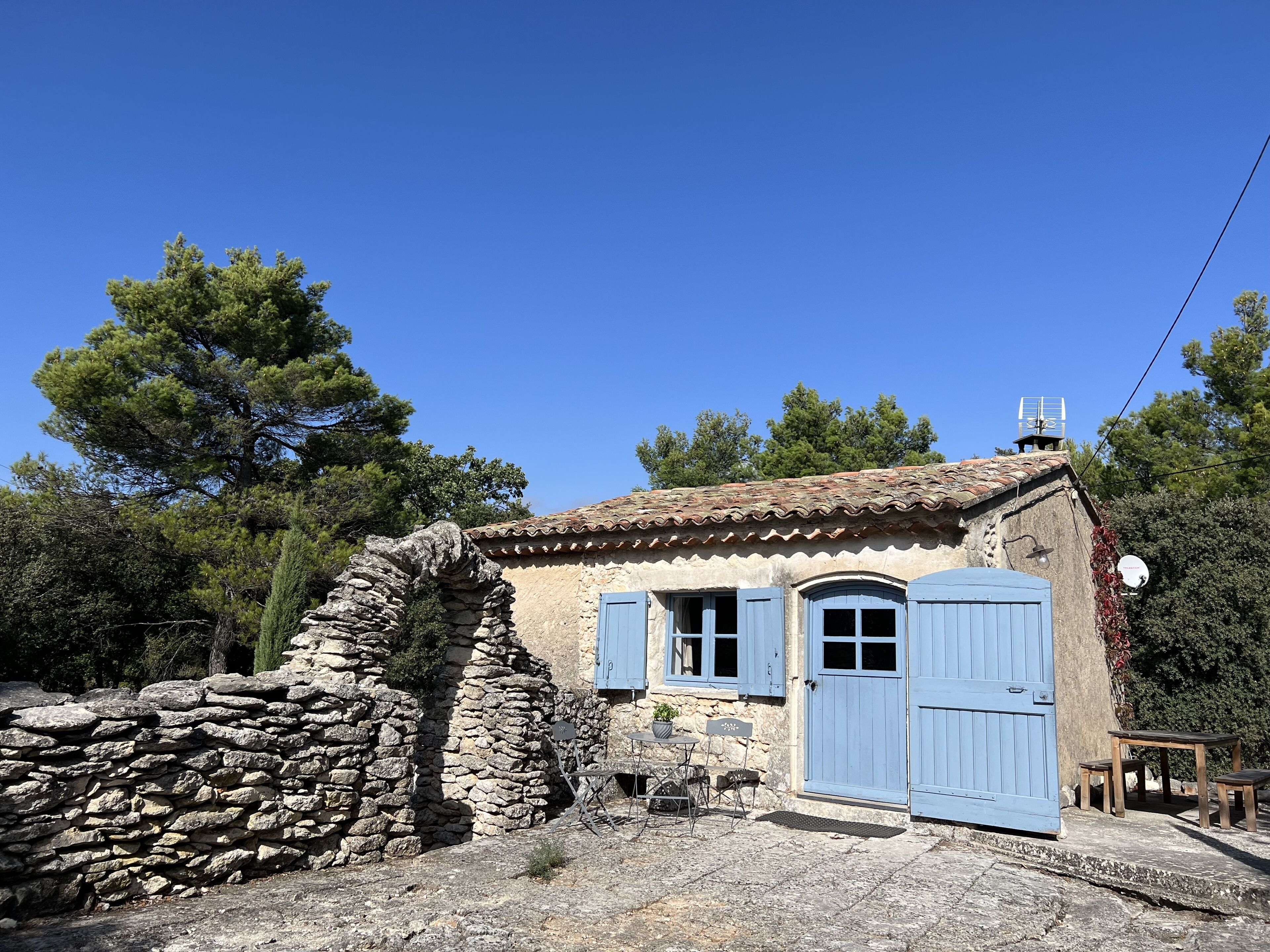 A stone building with a tiled roof, a blue door, and a small outdoor seating area.