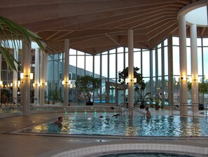 An indoor swimming pool with multiple lanes, surrounded by large windows and columns, and equipped with underwater lighting.
