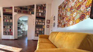 Una sala de estar con un sofá amarillo, una estantería grande y un tapiz colorido en la pared.