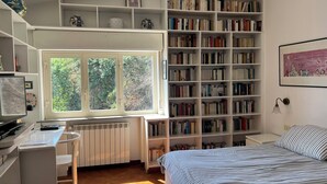 Un dormitorio con un ventanal grande, una estantería, un escritorio y una cama.