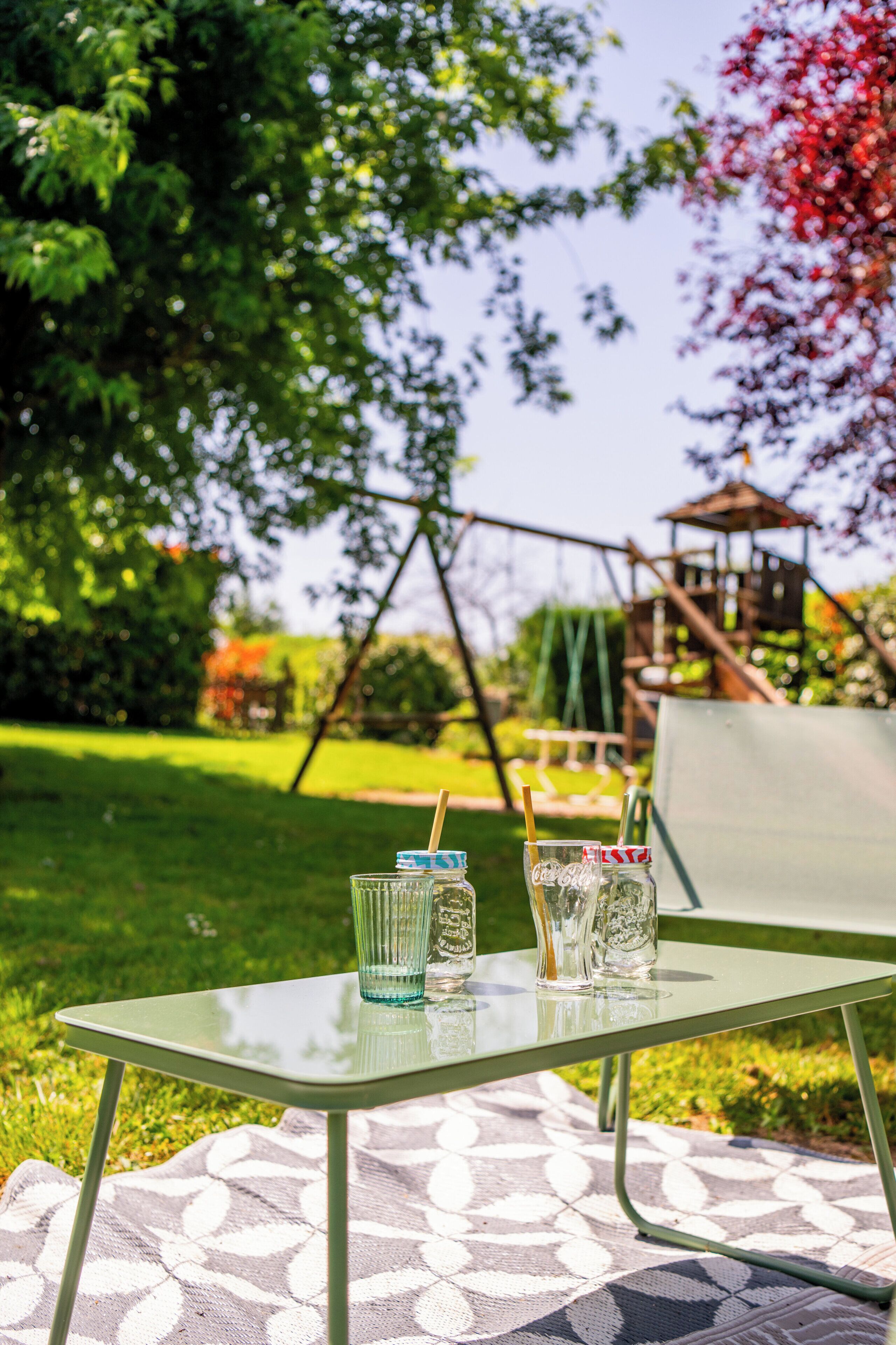 Une table en verre avec des boissons, et un portique à balançoire en arrière-plan.