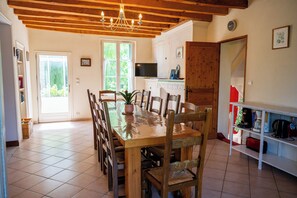 A dining area with a wooden table and chairs, a chandelier, a television, and a kitchen area with cabinets and appliances.