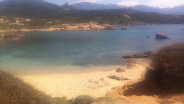 Eine Küstenlandschaft mit klarem Wasser, Sandstrand und Bergen in der Ferne.