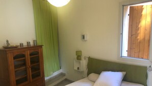 Ein Schlafzimmer mit einem Bett, einem Holzschrank, einem grünen Vorhang und einem Fenster mit Holzjalousien.