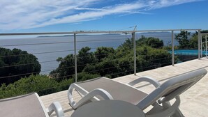 A balcony with a view of a large body of water and distant land. - Beautiful sea view - Spacious and comfortable - Walking distance to the beach (Le Lavandou)