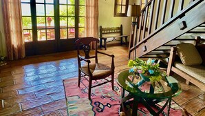A spacious room with a wooden floor, a large window with curtains, a wooden bench, a table with a vase of flowers, and a staircase with a railing. - Provençal villa with sea views & Mediterranean garden, beaches, Wi-Fi, A/C (La Croix-Valmer)