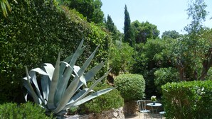 A garden with a stone wall, a large agave plant, and a small table with chairs. - Provençal villa with sea views & Mediterranean garden, beaches, Wi-Fi, A/C (La Croix-Valmer)