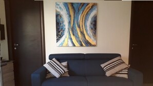 A dark blue sofa with striped pillows against a white wall, with a colorful abstract painting above it. - CORSE APARTMENT DUPLEX 6 PEOPLE  (Palasca)