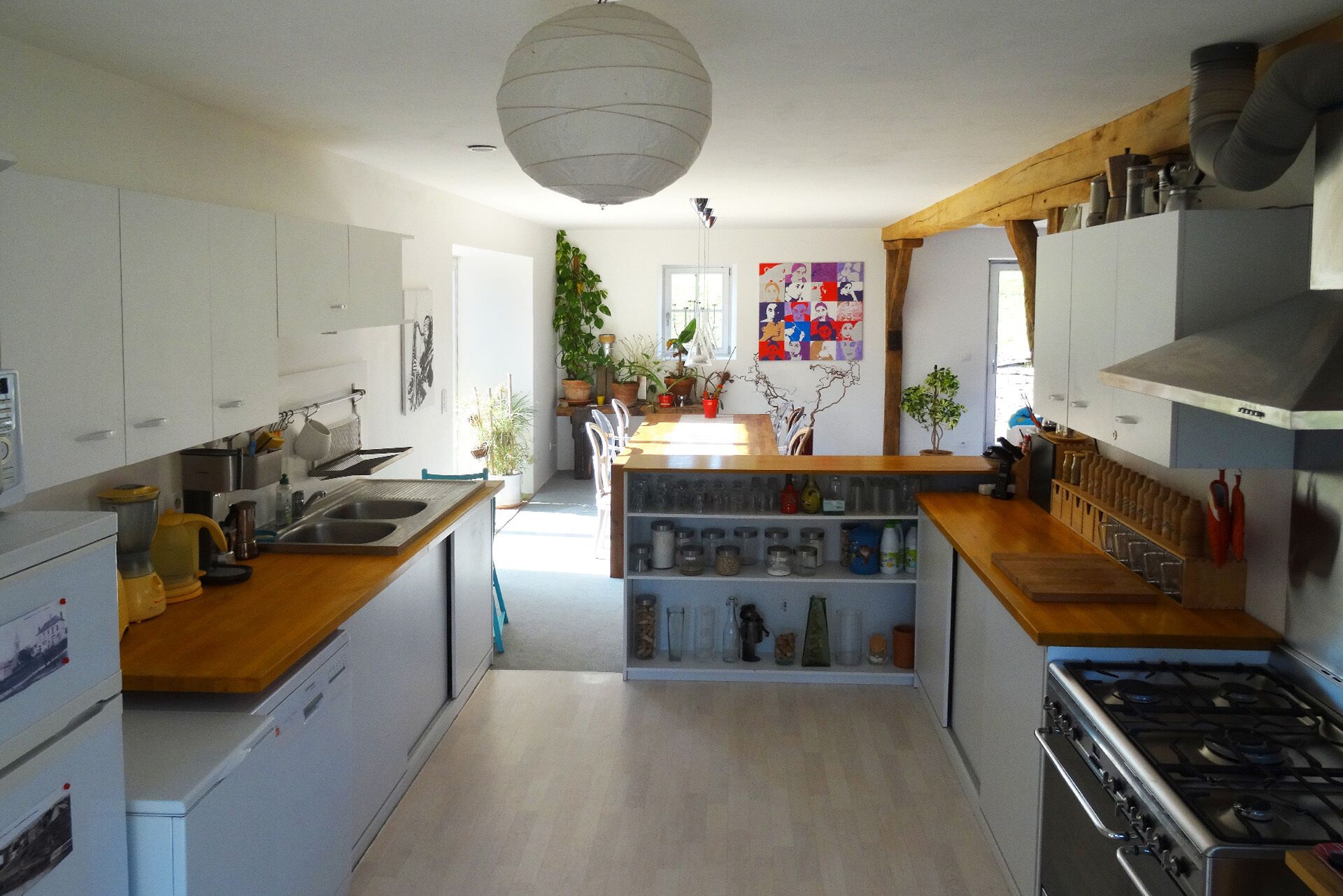 Una cocina moderna con armarios blancos, encimera de madera y estufa integrada. Se observan varios electrodomésticos y una planta en maceta.