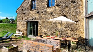 A stone building with a patio area featuring a grill, outdoor seating, and a large umbrella.