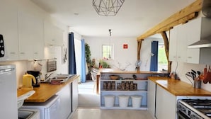 A modern kitchen with white cabinets, a wooden countertop, a built-in stove, and a ceiling light fixture.