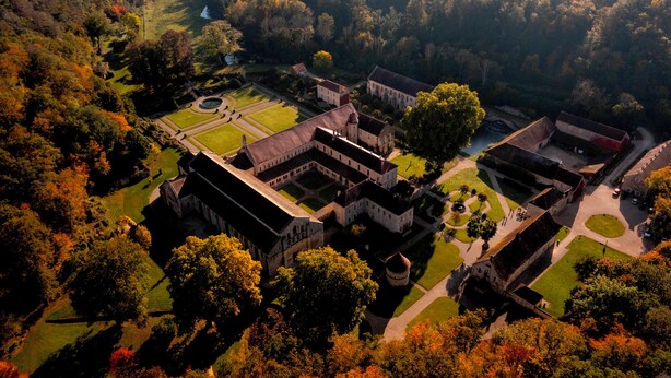 An aerial view of a historic estate with multiple buildings, manicured gardens, and a river.