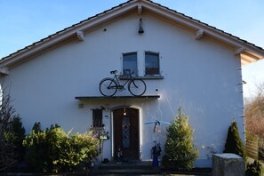 A house with a bicycle mounted on the wall above the front door, a small porch area, and a snow-covered stone.
