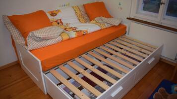 Een eenpersoonskamer met een houten bedframe, oranje beddengoed en een raam met uitzicht op buiten.