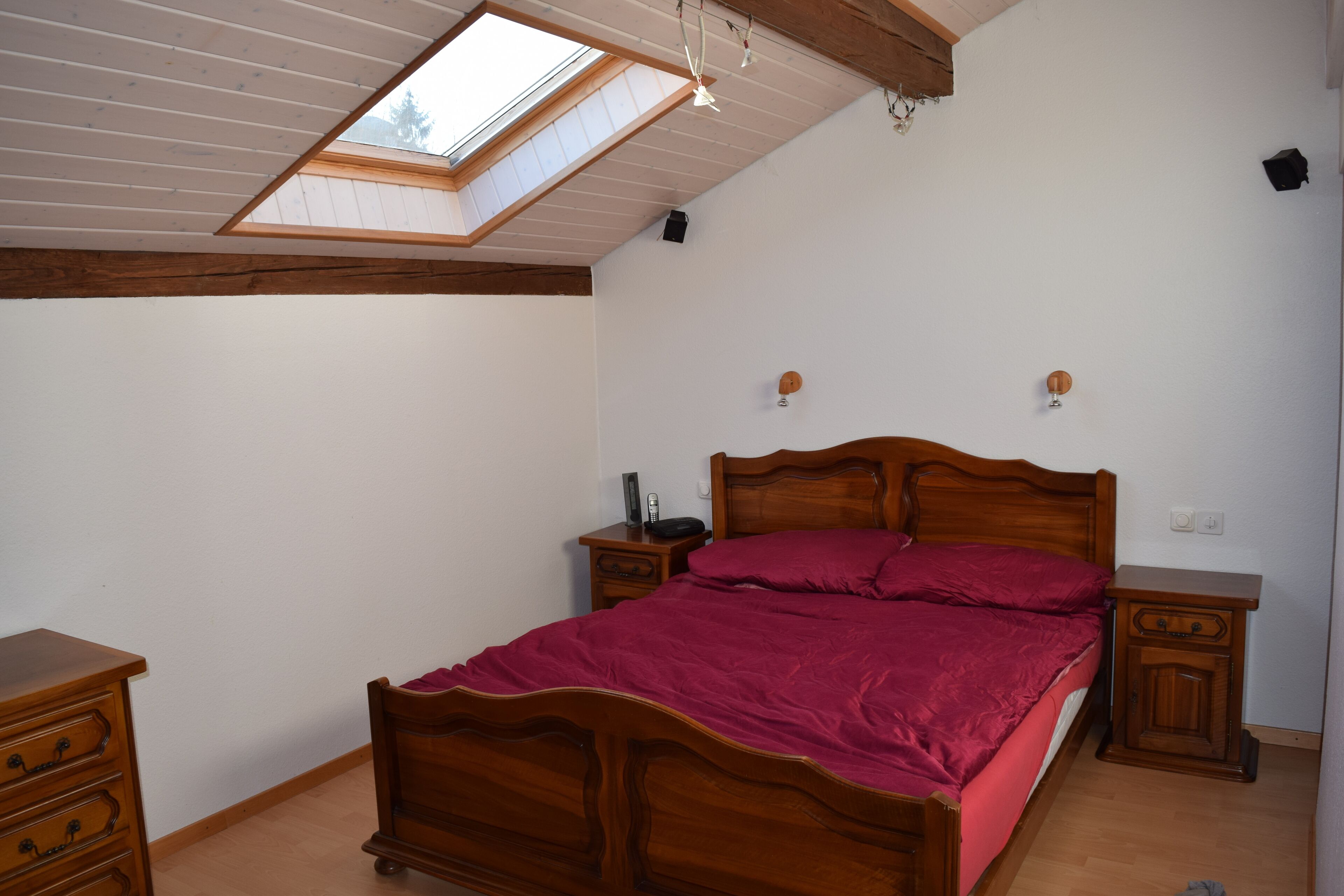 Une chambre à coucher avec un puits de lumière, un lit en bois, des tables de chevet et une commode.