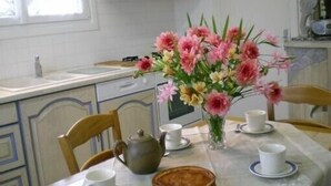 Een keuken met een eettafel gedekt voor twee personen, een bloevas en een theepot.