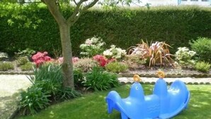 Een blauwe glijbaan voor kinderen in een tuin met verschillende planten en een boom.