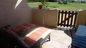 Une terrasse avec un banc rembourré, une table et un parasol violet.