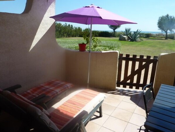 A patio with a cushioned bench, a table, and a purple umbrella.