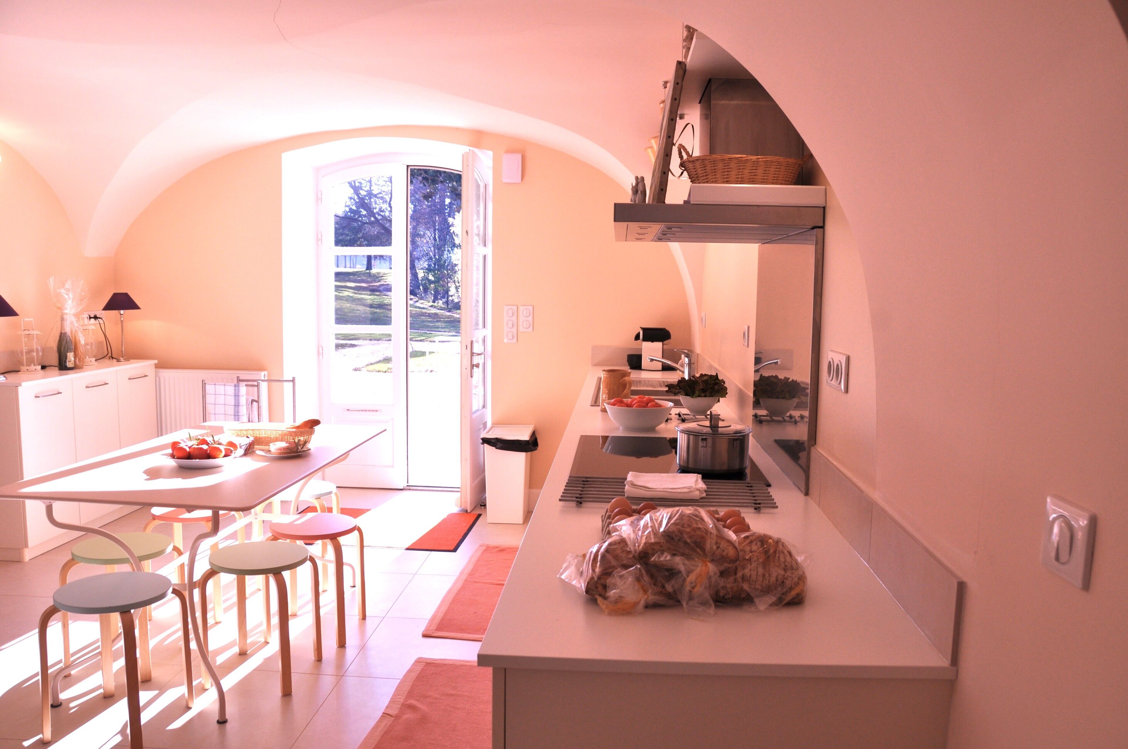 A modern kitchen with a large island, a dining area with chairs, and a view of the outdoors through a glass door.