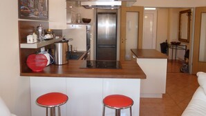 Eine moderne Küche mit einem Edelstahlkühlschrank, einem Gasherd und einer Kaffeemaschine. Zwei rote Barhocker und ein Stadtbild an der Wand.