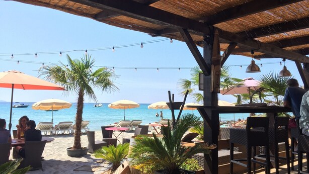 Ein Sitzbereich im Freien mit Sonnenschirmen und Stühlen mit Blick auf Strand und Meer.